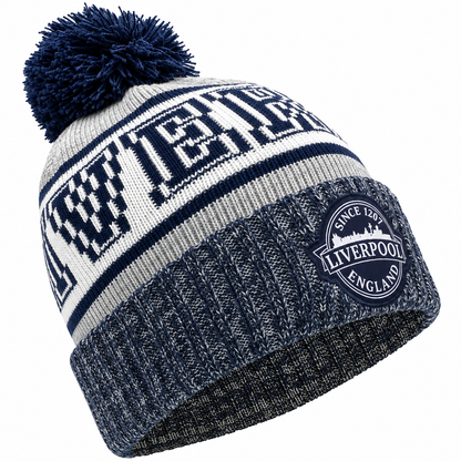 A navy blue and white knit beanie with a large pom-pom on top. The front has a bold navy and white striped pattern with the word 'LIVERPOOL' in large block letters, and a circular embroidered patch on the cuff that reads 'SINCE 1897 LIVERPOOL ENGLAND'.