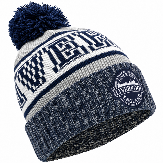 A navy blue and white knit beanie with a large pom-pom on top. The front has a bold navy and white striped pattern with the word 'LIVERPOOL' in large block letters, and a circular embroidered patch on the cuff that reads 'SINCE 1897 LIVERPOOL ENGLAND'.