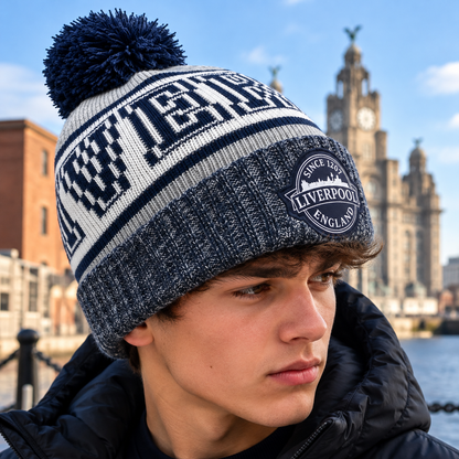A close-up of a young man wearing a navy and white knit beanie with a pom-pom. The beanie features the words 'LIVERPOOL' and a circular 'Liverpool England' patch on the cuff.