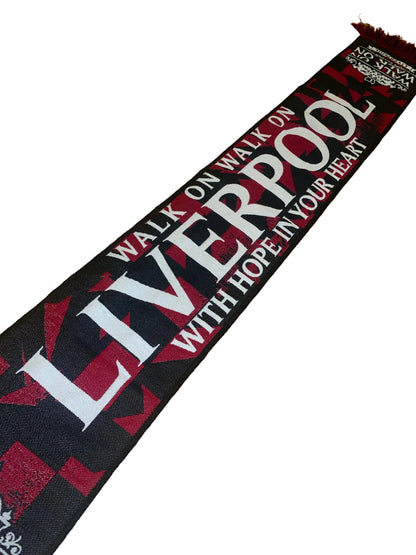 A black and red Liverpool FC scarf with white text reading 'WALK ON WALK ON LIVERPOOL WITH HOPE IN YOUR HEART', laid diagonally on a wooden floor.