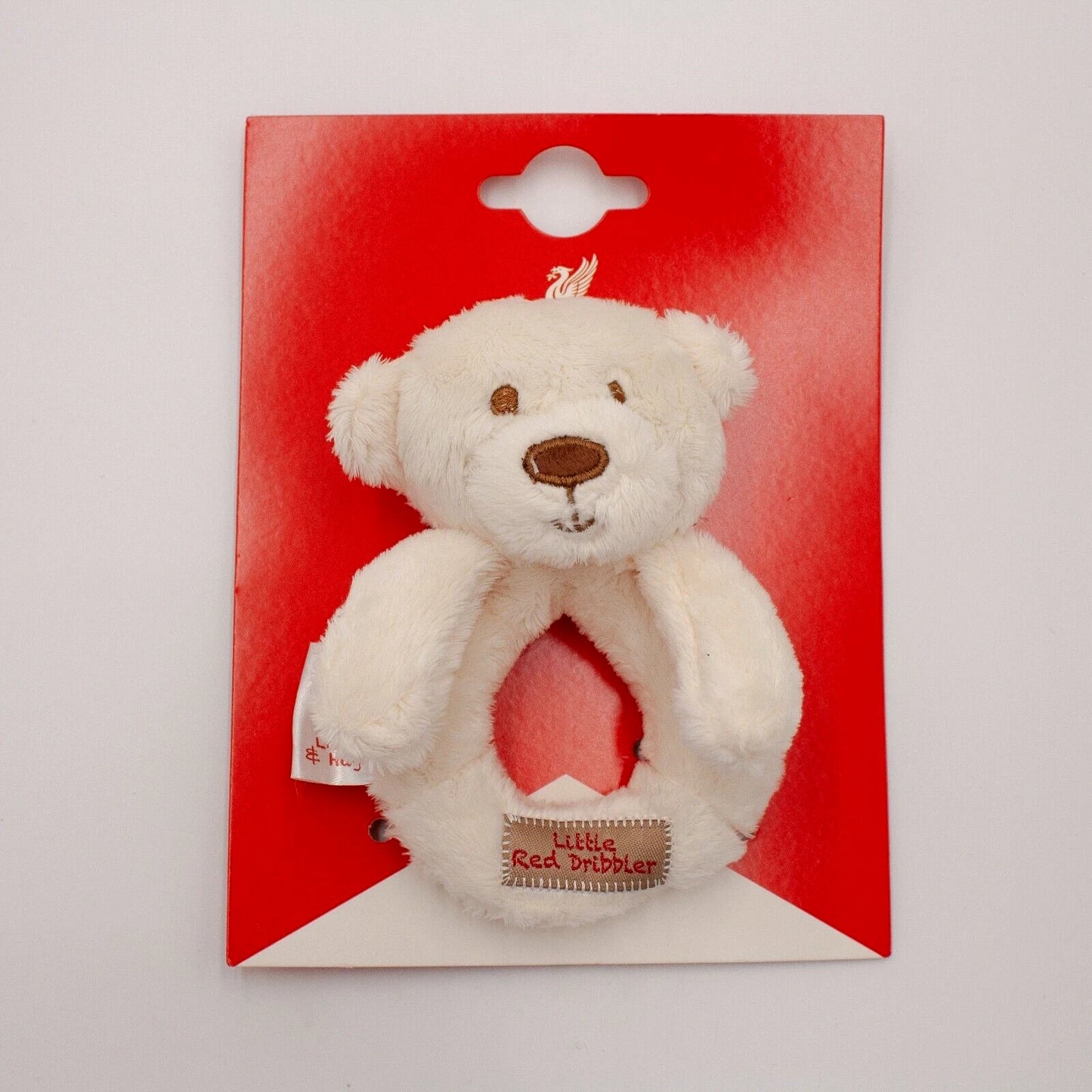A plush white teddy bear ring with a brown embroidered nose and eyes, attached to a red cardboard backing card with a hanging hole, photographed against a light gray background.